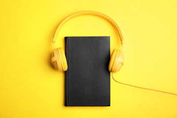 Book and modern headphones on yellow background, top view