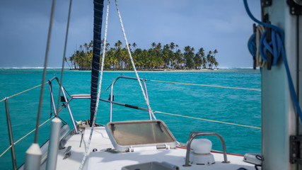 A beautiful Deserted Tropical Island overgrown with green Palm Trees seen from a white Sailboat...