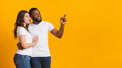 Joyful multiracial couple hugging and pointing aside at copy space