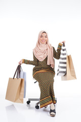 A beautiful Muslim female college student in a Asian traditional dress modern kurung carrying shopping bags isolated on white background. Eidul fitri fashion and festive shopping concept.