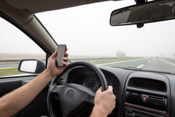 Use of smartphone in car. Man using phone while driving in fog on highway.