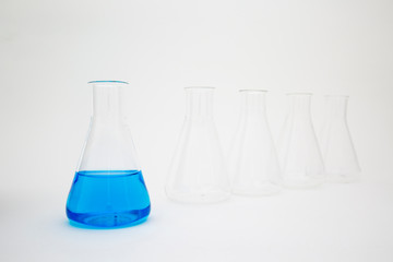 Scientific laboratory glass erlenmeyer flask filled with blue liquid with glassware equipment on white background.