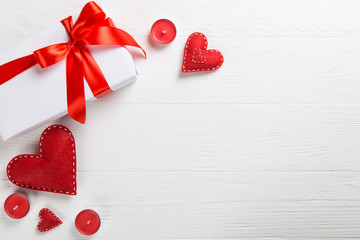 White packed gift with red ribbon, candles and handmade heart on the table. A romantic valentine's day surprise for a loved one.