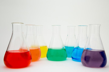 Scientific laboratory glass erlenmeyer flask filled with colorful liquid forming rainbow on white background.