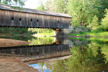 Old New England covered bridge over calm river. Reflection of bridge in water 