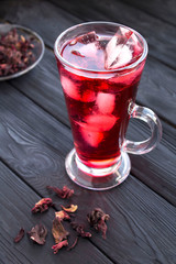 Iced hibiscus or karkade tea in the glass on the black wooden  background. Location vertical. Closeup.