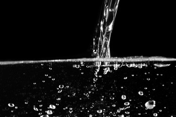Naklejka na ściany i meble Stream of water pouring into water at black background. Close up.