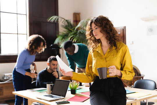 Woman with paper and coffee cup in office with colleagues in background
