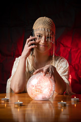 Fortune Teller with Crystal Ball and mobile phone on table with candles. Smartphone, online or call...