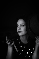  woman on a blurry black background looks at her watch and holds a hat in her hand. black and white image. grain.