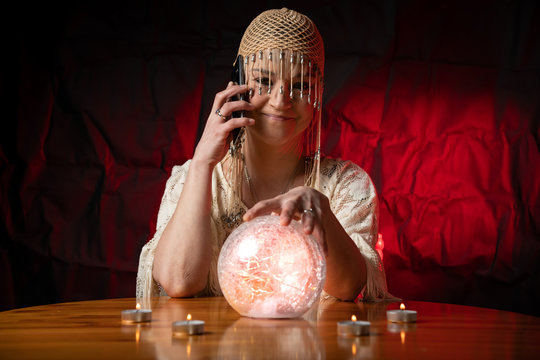 Fortune Teller with Crystal Ball and mobile phone on table with candles. Smartphone, online or call concept