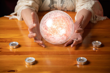 Fortune Teller with Crystal Ball on table with candles and black and red mottled background