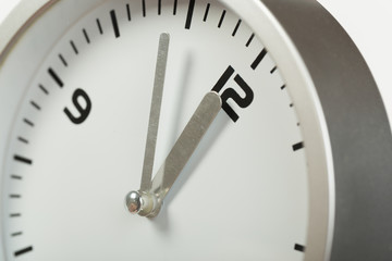 5 minutes to 12 white with light metal minimalistic clock close-up on a light background