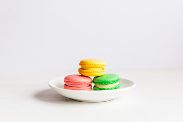 Three tasty french macarons on a white plate and wooden table. Pink, yellow and green macarons.