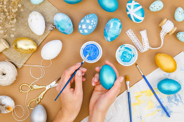 Handmade crafting Easter decorations. Top view woman painting in a gold and blue colors easter eggs