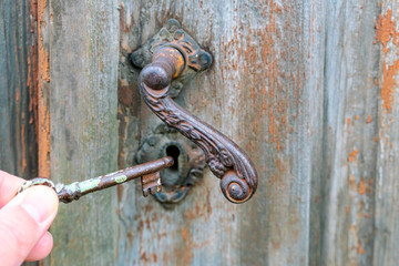 Hand holding metal vintage key to unlocking old wooden door, film tone color. Antique door lock and key.