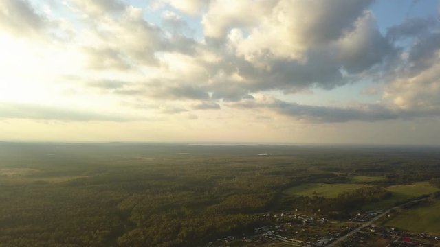 Aerial panorama of a vivid landscape with village, fields, forests and a beautiful bright blue sky with white clouds. Stock footage. Flying over the meadows and green pine tree dense forest.