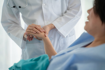 Medicine,health care and trust concept.Doctor holds the hand of a patient as a sign of care and consolation.Hand of doctor reassuring his female patient in bed at hospital.