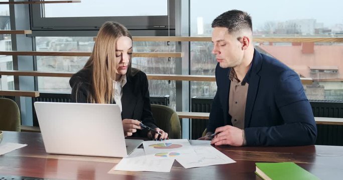 Man and a woman discussing work in the brightly lit modern office. Concerned male and female working with laptop, charts papers and handshaking. Business people discuss new startup project concept