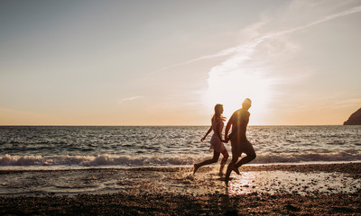 Young couple running at the beach during sunset