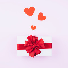 Gift with a red bow on a soft pink background with red hearts, for Valentine's day.