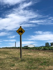 Yellow tractor crossing sign.  Farm and blue skies are visible in the background