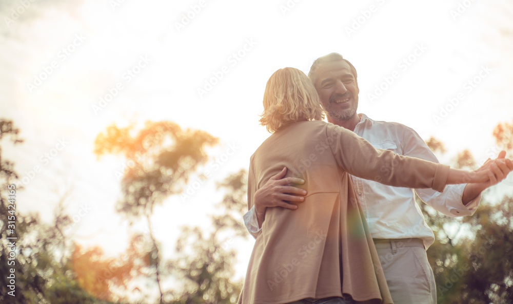 Wall mural Romantic and valentine concept.Senior active caucasian couple dancing and holding hands looks happy in the park in the afternoon autumn sunlight,bokeh,anniversary,happily retired with copy space.