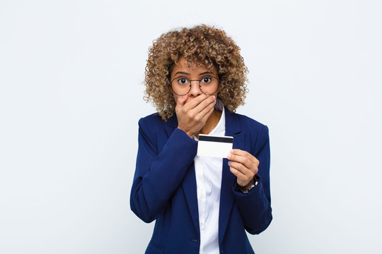 young african american woman covering mouth with hands with a shocked, surprised expression, keeping a secret or saying oops with a credit card