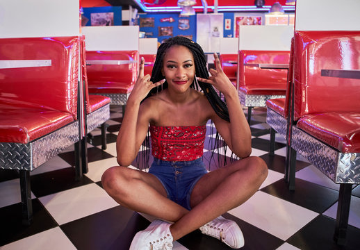 Young woman with braided hairstyle sitting on the black and white floor of an american diner restaurant