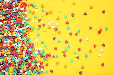 Colorful heart shaped sprinkles on yellow background