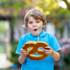 Adorable little kid boy eating huge big bavarian german pretzel. Happy blond child enjoying tasteful tratditional bread. Healthy food for happy kids