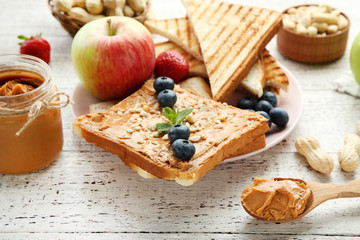 Bread with peanut butter, fruits and nuts on white wooden table