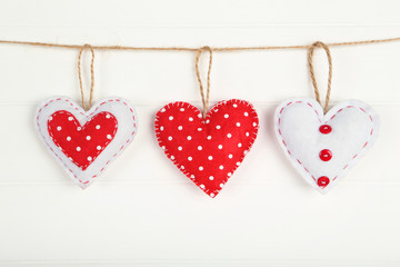 Fabric hearts hanging on white wooden background