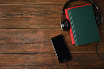 Books, mobile phone and headphones on wooden table, flat lay. Space for text