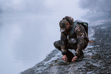 Naklejka premium Fisher man fishing with spinning rod on a river bank at misty foggy winter, spin fishing, prey fishing