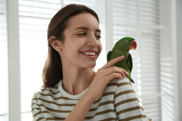 Fototapeta premium Young woman with cute Alexandrine parakeet indoors