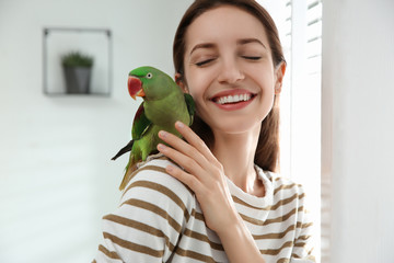Young woman with cute Alexandrine parakeet indoors © New Africa
