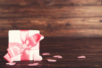 Gift box with ribbon and hearts on brown wooden table