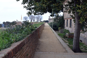Fototapeta na wymiar Long Narrow Walkway alongside Old Brick Wall with flowers in Ancient Fortress