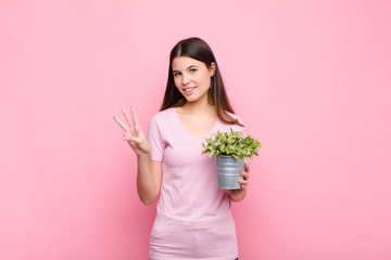 young pretty woman smiling and looking friendly, showing number three or third with hand forward,...