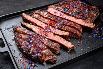 Modern design barbecue dry aged wagyu flank steak offered with herb and salt as closeup on a modern design tray