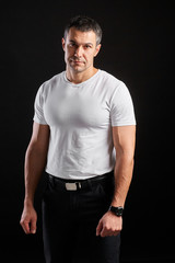 Handsome Athletic man in white blank t-shirt standing on black wall background