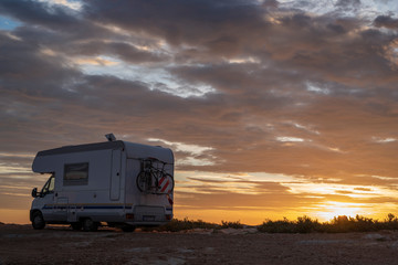 sunset / sunrise at rocky seaside with travel trailer with bike. Dramatic and calm cloudy sky with sun beams