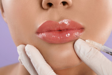 Young woman getting lips injection on lilac background, closeup
