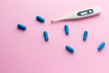 Digital thermometer and blue pills isolated on pink background. Epidemic, painkillers, healthcare and treatment concept. Flat lay. Top view with copy space.