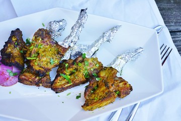 A platter of grilled lamb chops wrapped in aluminum foil at an Indian restaurant