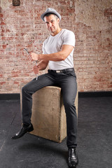 Athletic man with wrench on a brick background. Not a typical worker, in a white t-shirt and trousers.