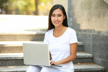 Beautiful young woman with laptop computer sitting on the step