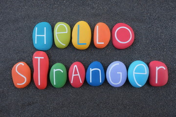 Hello stranger, english phrase composed with colored stone letters over black volcanic sand 