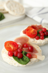 Puffed rice cakes with prosciutto, berries and basil on plate, closeup